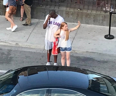 Woman hails a cab for a man wearing a Chicago Cubs jersey and holding a white cane. 